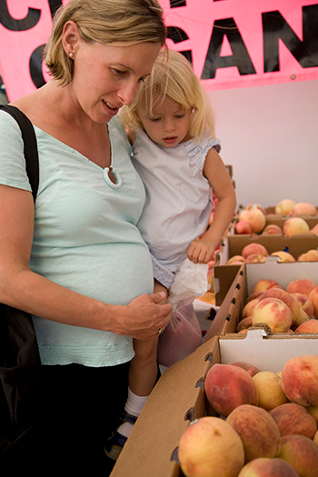 A woman and child at a fruit stand looking at boxes of peaches
